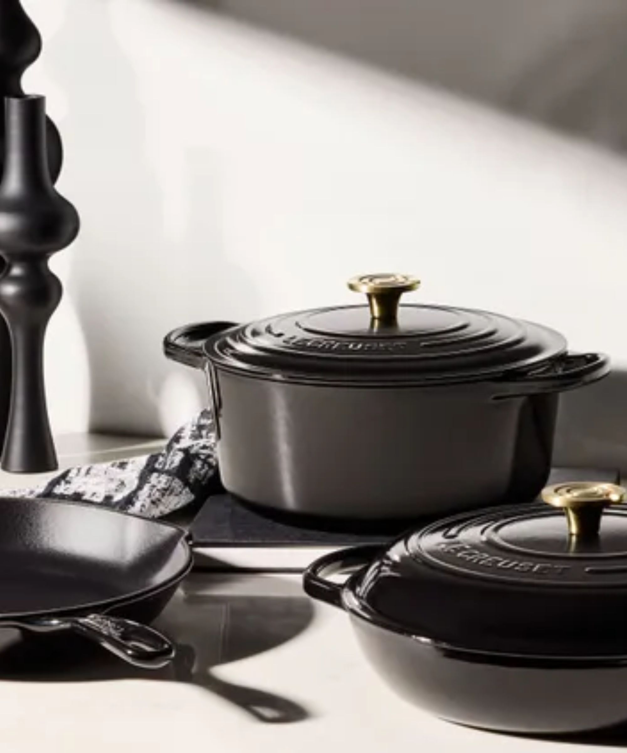 A polished jet black Le Creuset Dutch oven beside a shallow ban and frying pan