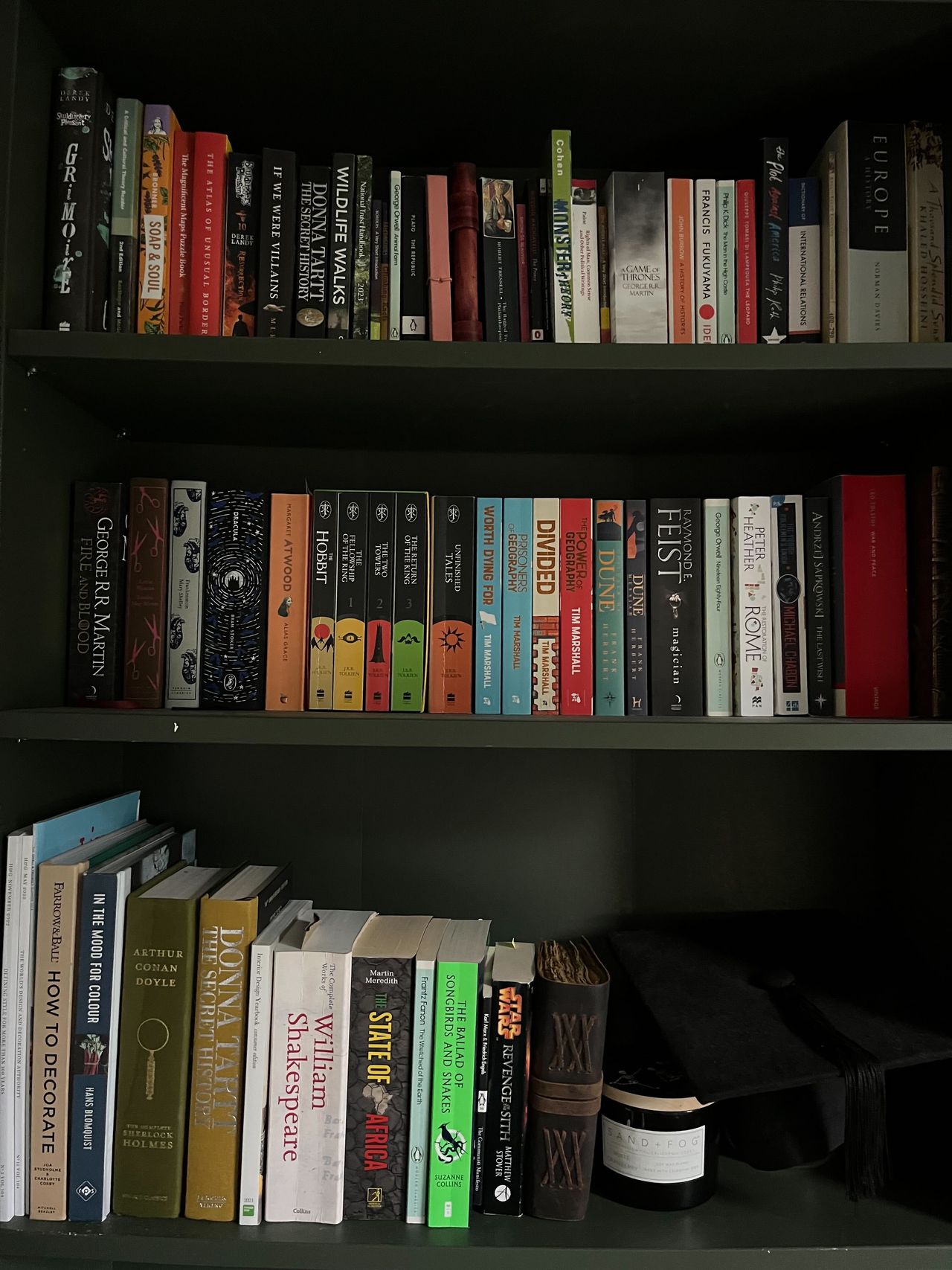 A dark green painted bookshelf with lots of books on it, neatly organzied
