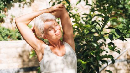 Woman stretching in back garden, wearing active clothes and with closed eyes, before doing a 10-minute abs workout