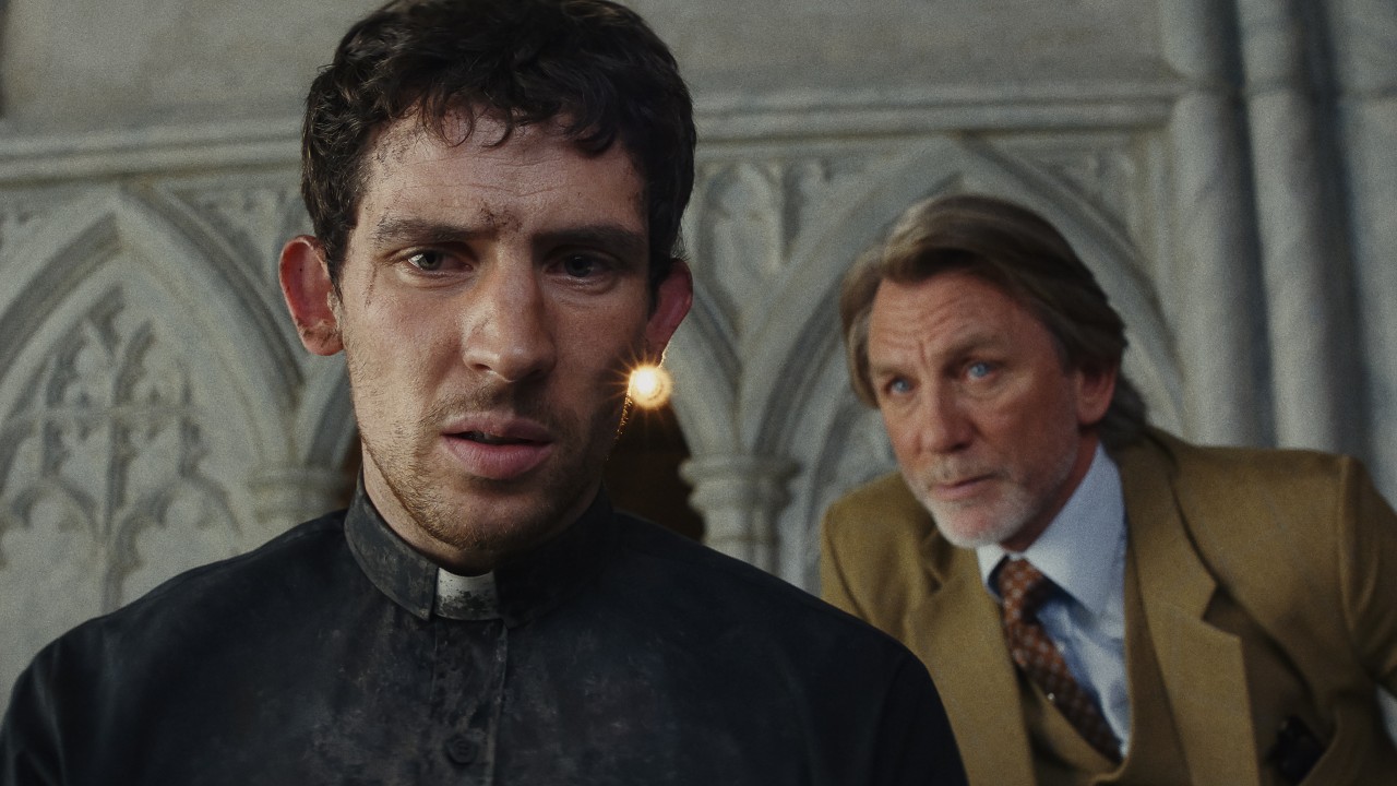 The priest looks on while Benoit Blanc watches