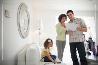 Couple looking at energy bills at home while daughter plays on sofa