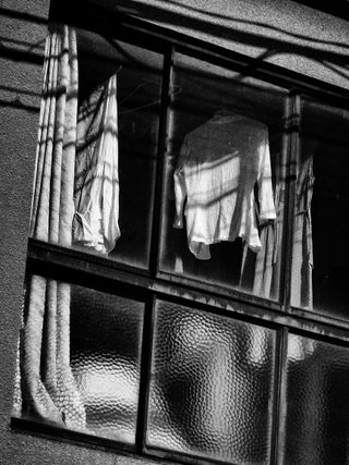 Black and white photograph of clothes hanging in a window.