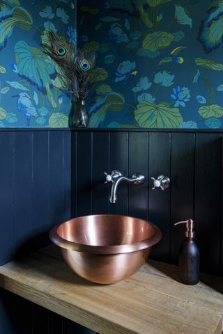 dark blue paneling in bathroom with peacock wallapper and copper basin