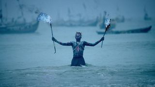 Man standing in the sea holding blue flaming torches