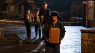 Reggie walks home in the dark carrying a box while a gang of boys stand behind him