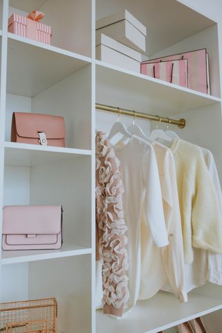 Neutral colored clothing hanging neatly in a white closet space