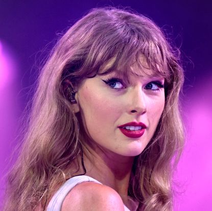 Taylor Swift on stage in a purple dress with purple lights behind her