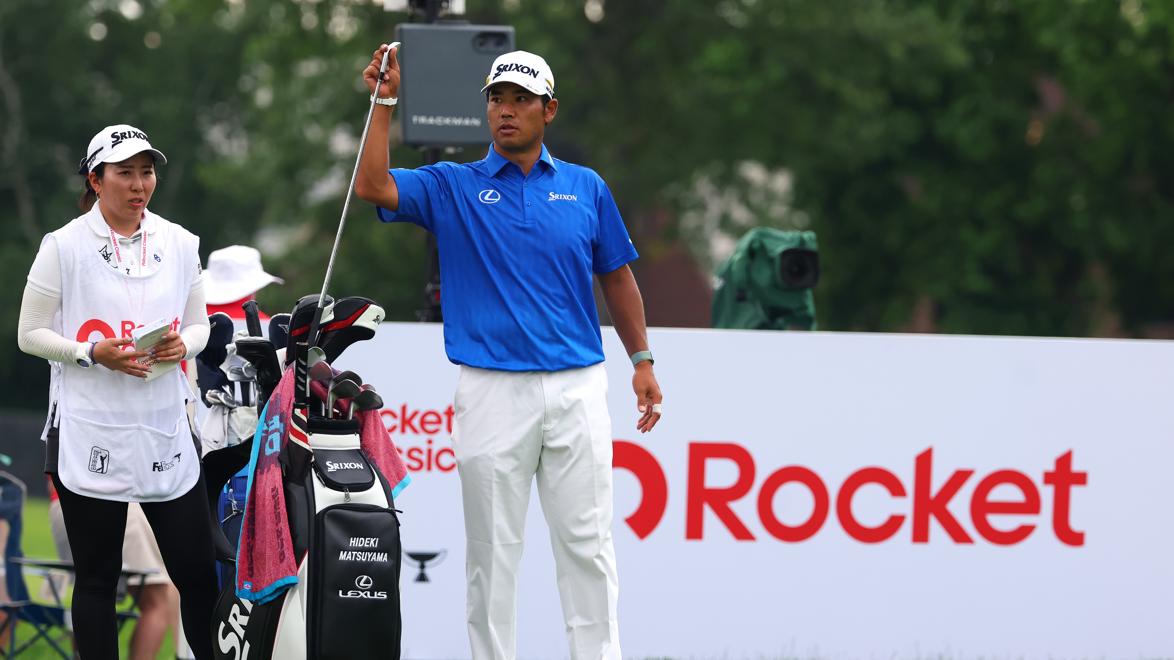 Hideki Matsuyama picking out a club with caddie Mei Inui standing on the tee at the 2025 Rocket Classic