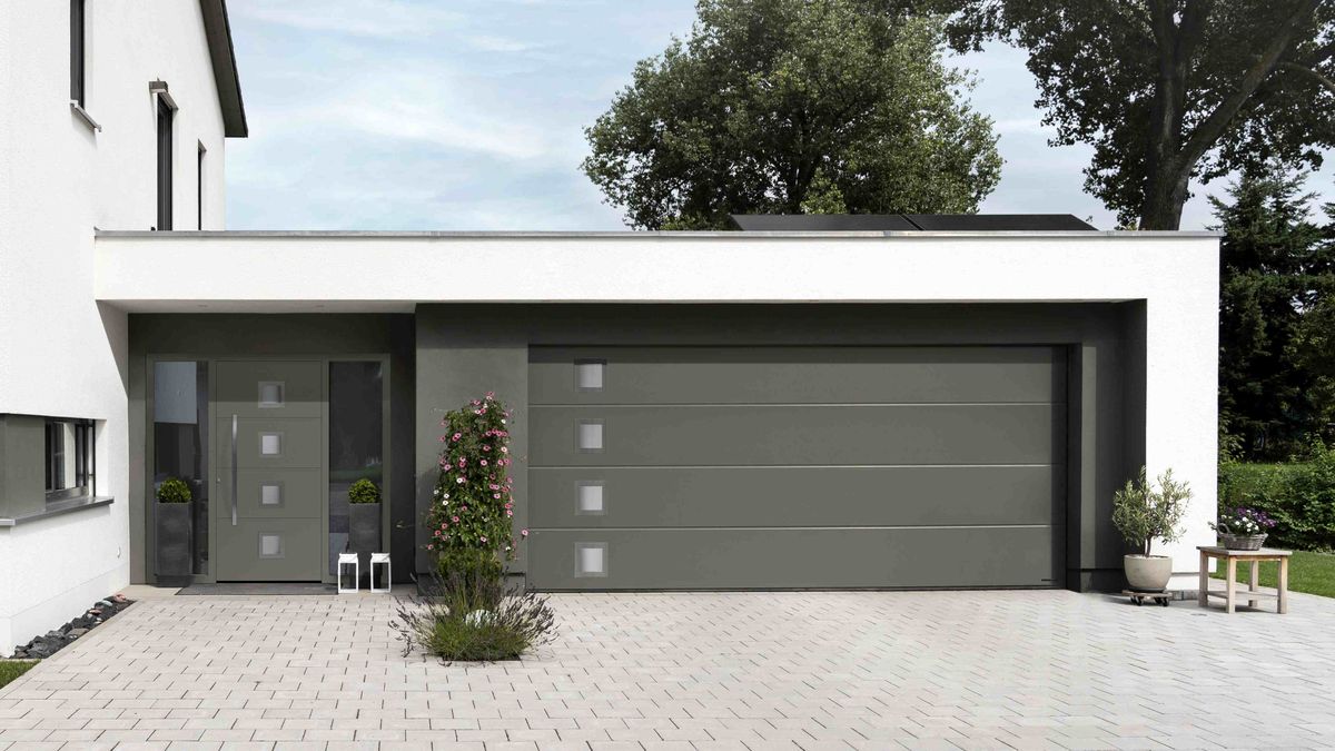 A modern white-rendered house with large single-storey garage. The garage features a large grey sectional garage door from Hörmann, together with a matching front grey front door from the company.