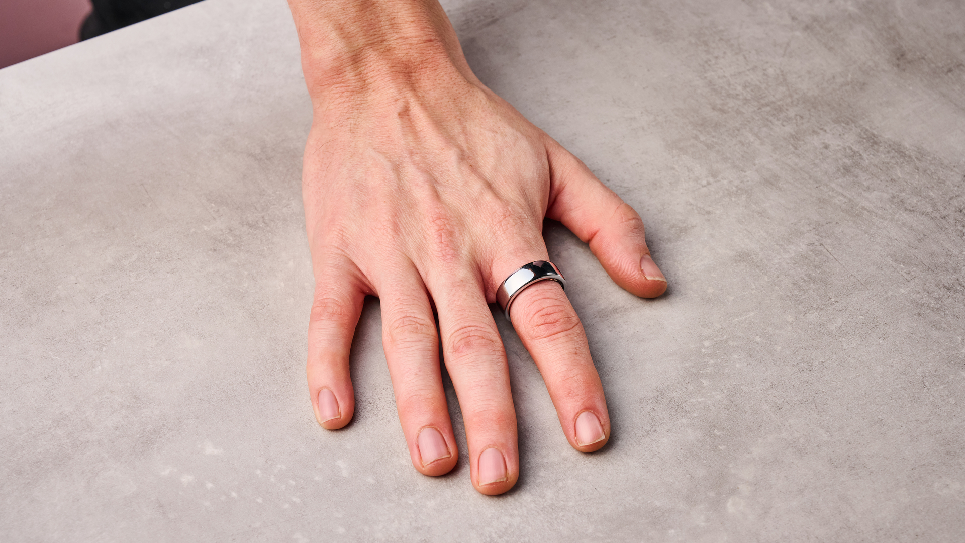 The Oura Ring 3 on a man's index finger as he lays his hand flat on the table.