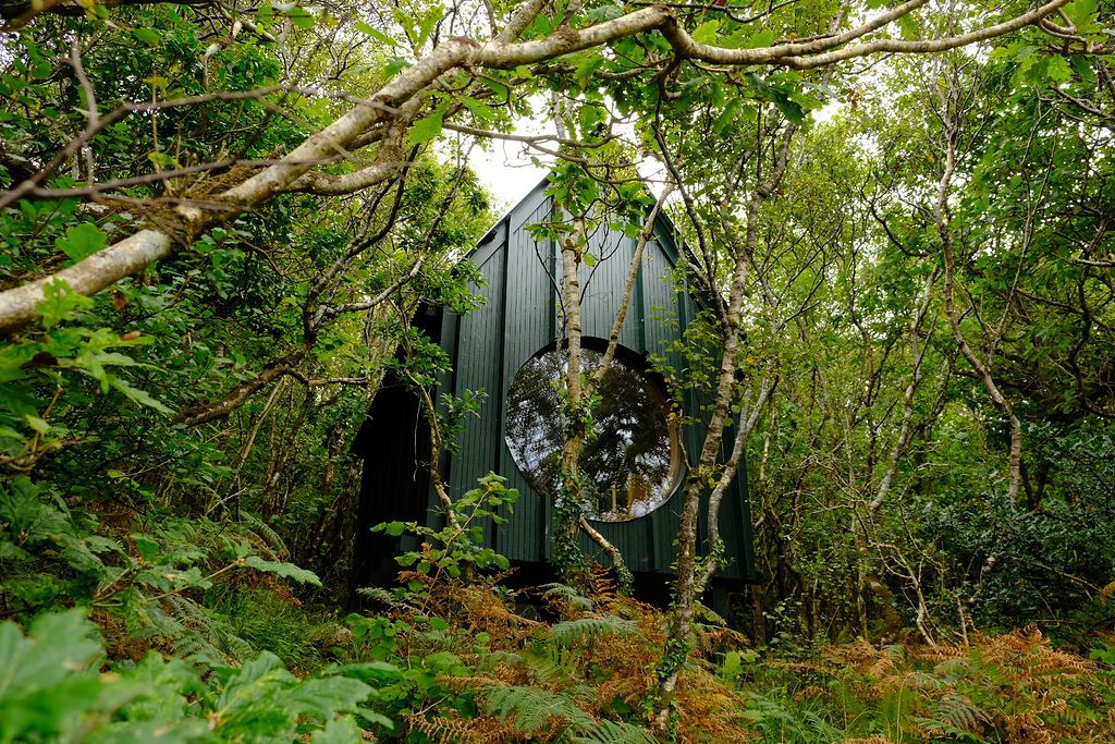 A greenery-immersed, architectural sauna boasts a porthole window that lets guests peek into nature while indoors, and the other way around.
