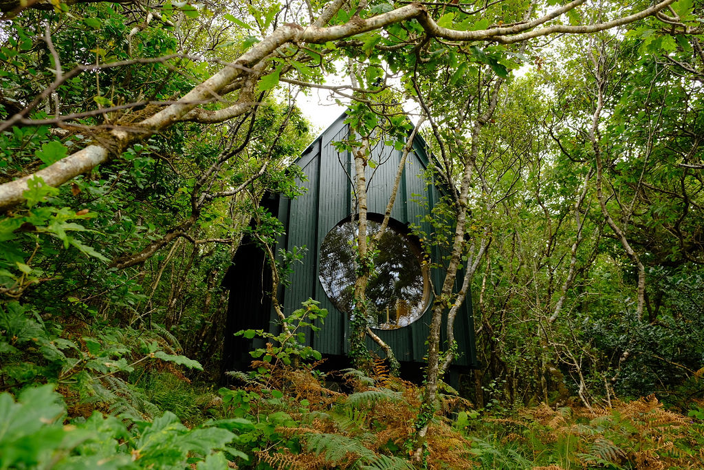 A greenery-immersed, architectural sauna boasts a porthole window that lets guests peek into nature while indoors, and the other way around.