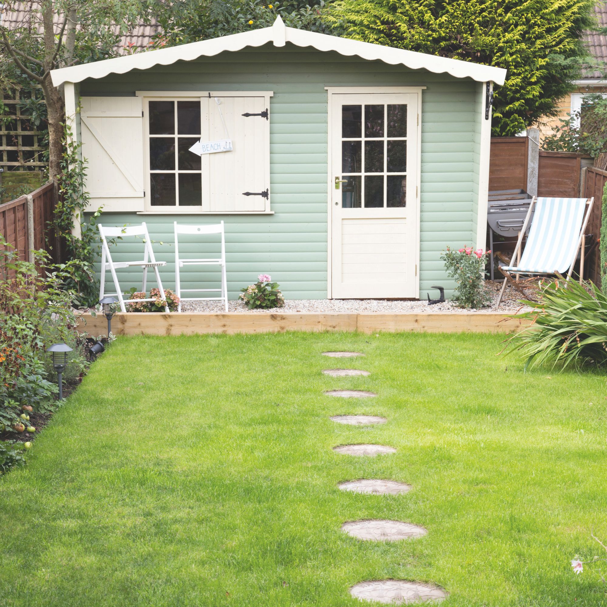 Green lawn with stepping stones leading to a large green and white shed
