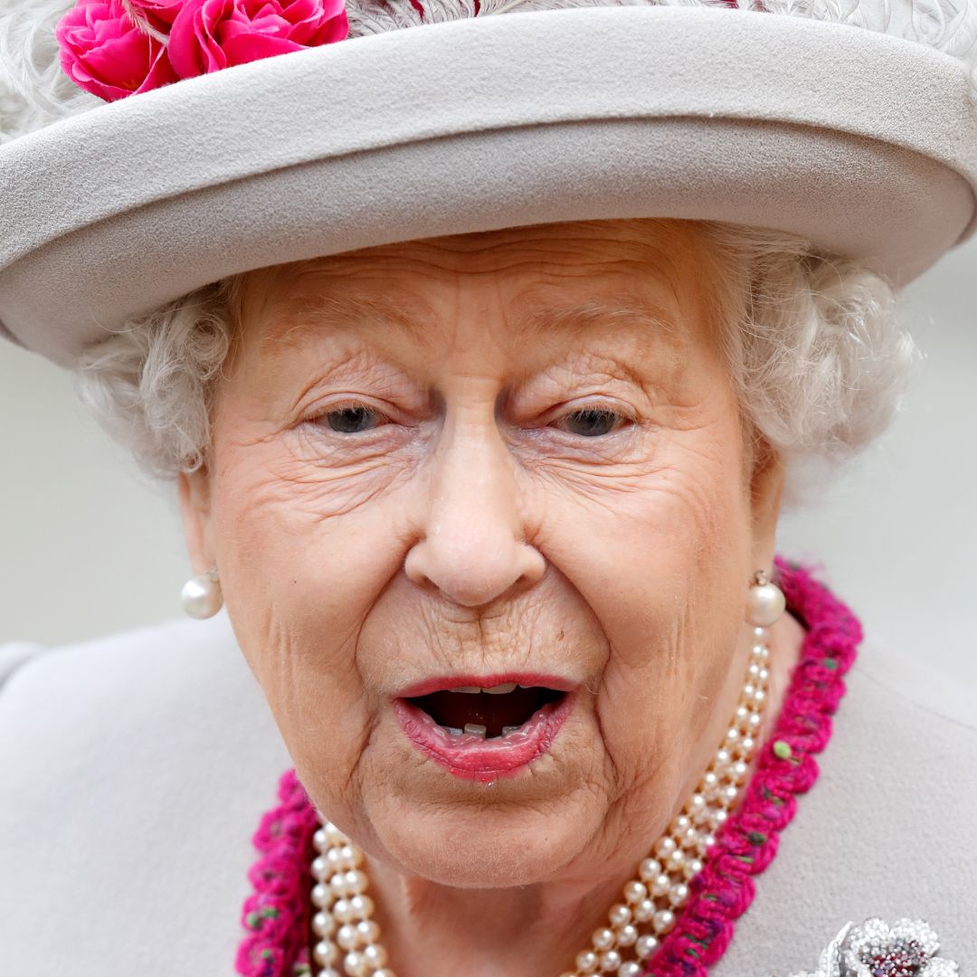 Queen Elizabeth looks shocked while wearing a gray and cerise coat and matching hat