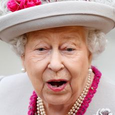 Queen Elizabeth looks shocked while wearing a gray and cerise coat and matching hat
