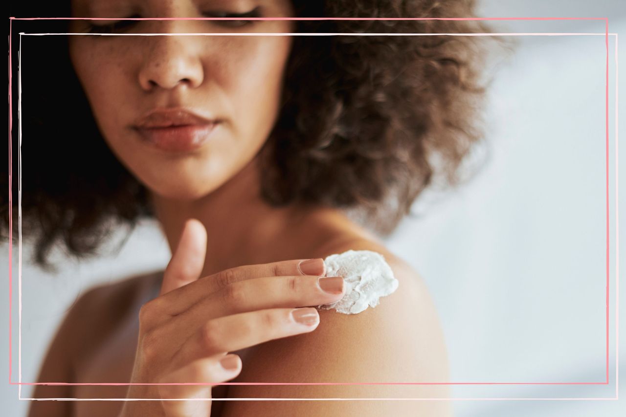 A woman looks down at her bare shoulder whilst applying a sudocream with her finger, following the doctor recommended advice for how to treat sunburn