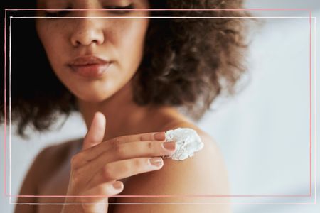 A woman looks down at her bare shoulder whilst applying a sudocream with her finger, following the doctor recommended advice for how to treat sunburn