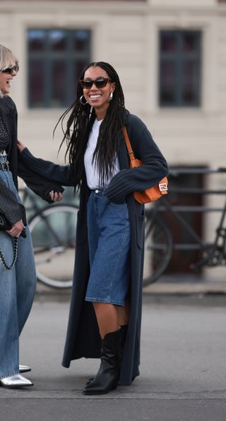 woman wearing coat, white t-shirt, bermuda shorts, and cowboy boots