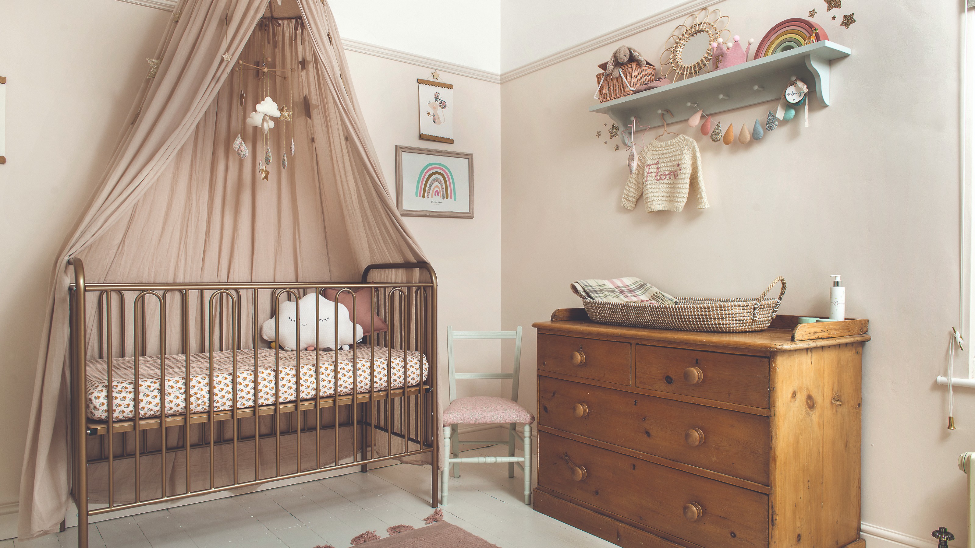 A nursery with a metal cot with a pink canopy and vintage wooden chest of drawers