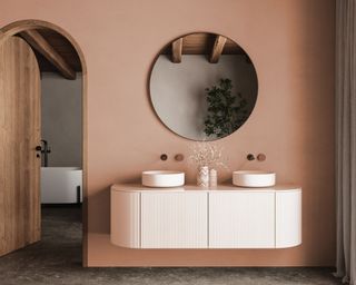 bathroom with terracotta walls, white vanity unit, circular wall mirror and double sinks