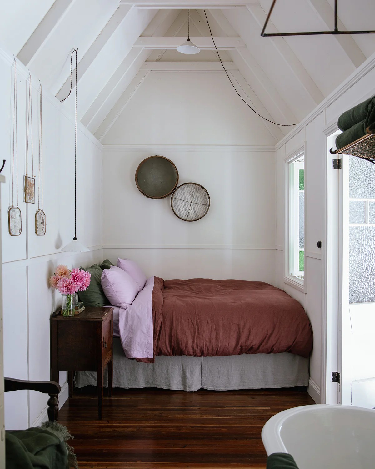 Image of a white bedroom with a the bed tucked into a nook. There is lilac, olive green, and terracotta bedding on the bed.
