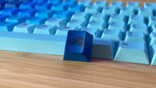 Glorious branded escape keycap in blue leaning against the rest of the Ocean set