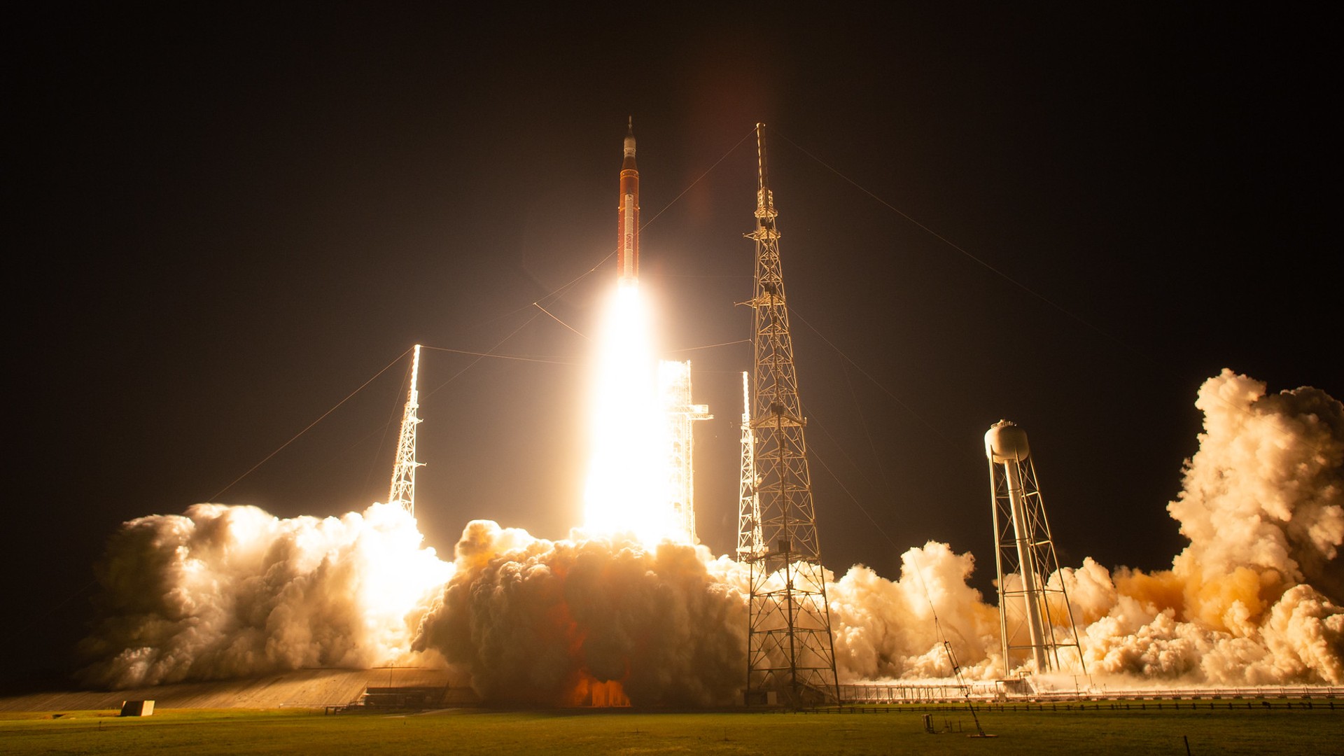 a rocket lifts off at night above a massive plume of smoke