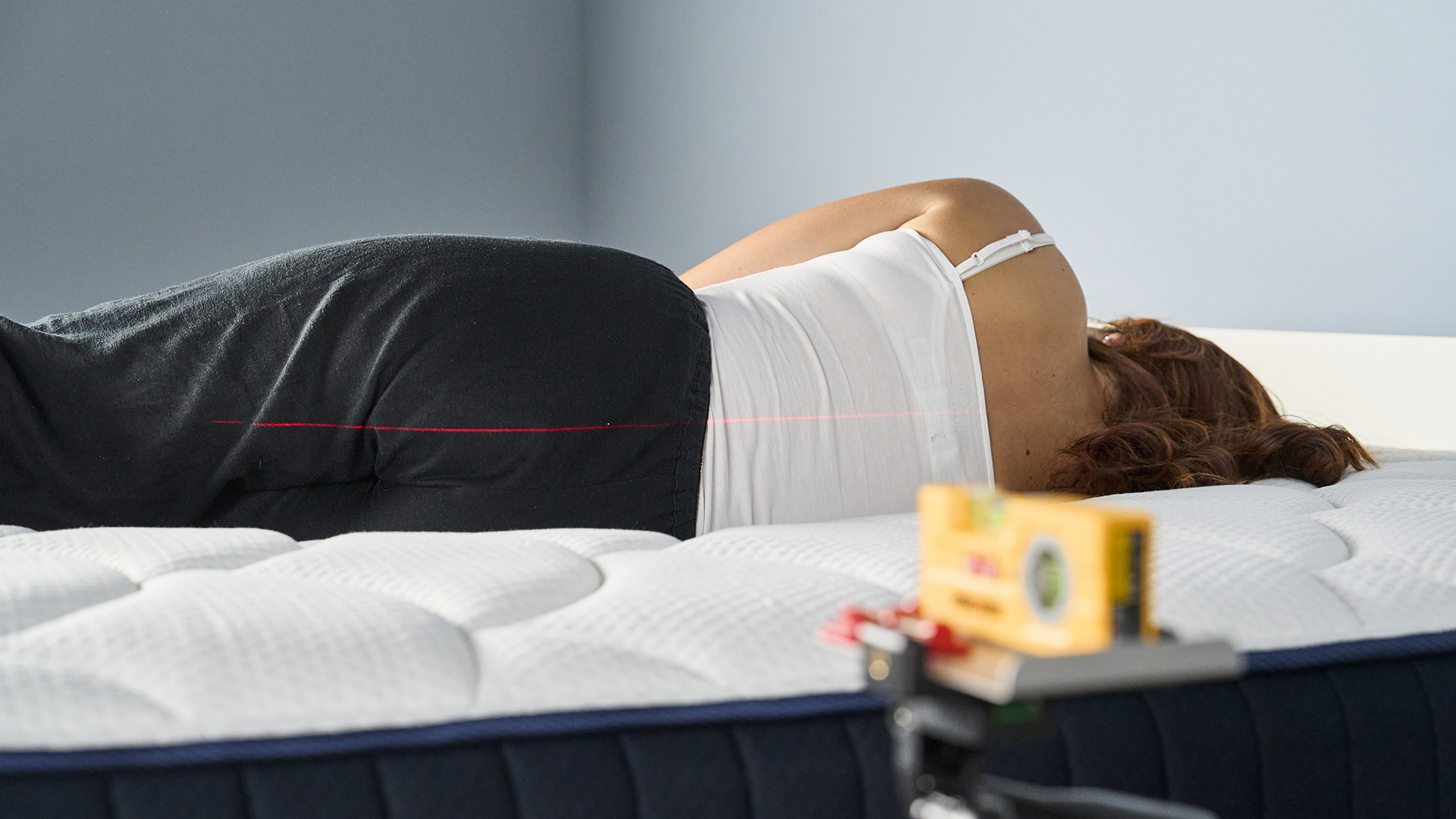A Tom&#039;s Guide tester lying on her side facing away from the camera while lying on the DreamCloud Classic mattress. A red laser can be seen along her back in a straight line to measure spinal alignment.