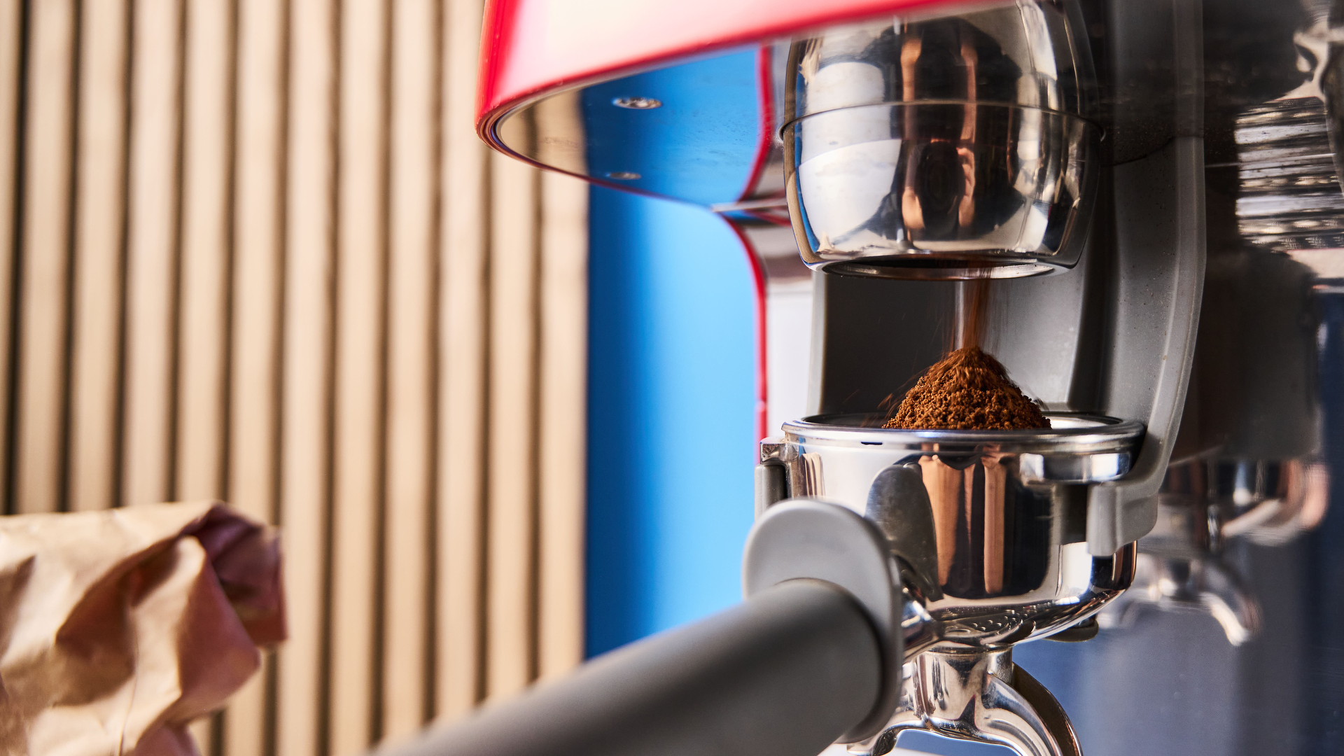 a red smeg espresso machine with burr grinder is photographed against a blue background
