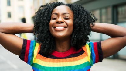 happy woman outside in rainbow shirt smiling and embracing main character energy 