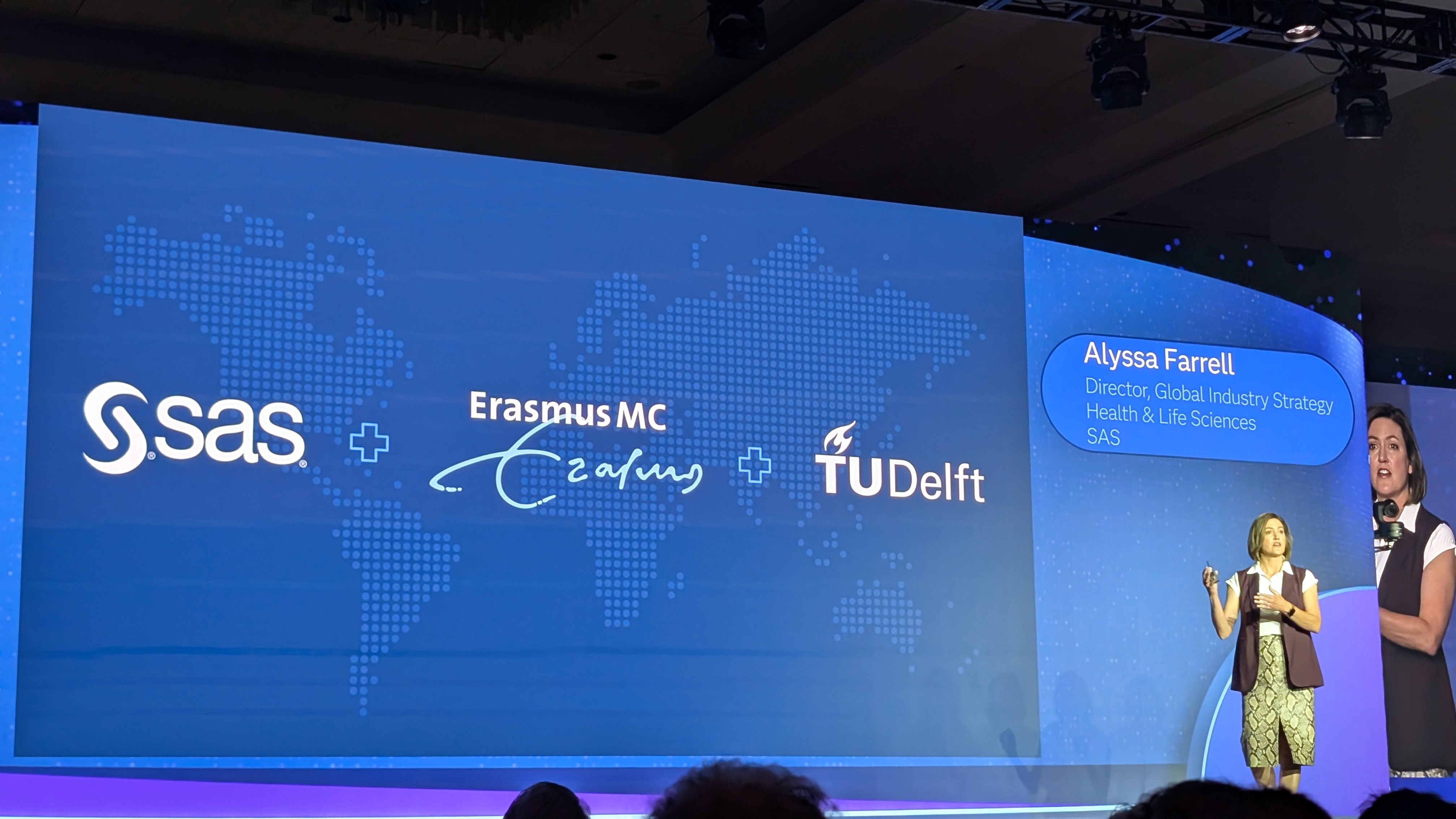 Alyssa Farrell, director, Global Industry Strategy Health & Life Sciences at SAS, onstage during the SAS Innovate 2025 day-two keynote next to a large screen showing the logos of SAS, Erasmus University Medical Center (Erasmus MC), and Delft University of Technology (TU Delft).