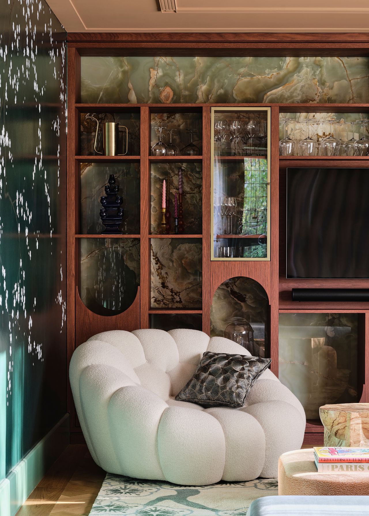 a corner of a living room with a backlit display cabinet and a shell-like cream armchair with a cushion in the corner