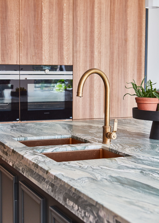 a leathered marble kitchen island with a double sink and a brass tap