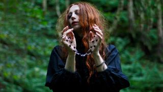 Darkher in a forest holding a rosary