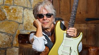 Johnny A. poses with a gold Strat-style guitar