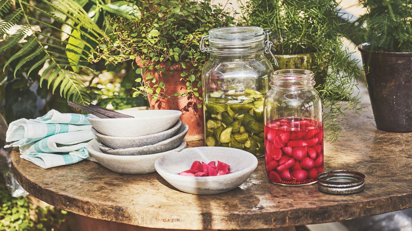 Mason jars with pickles in on a rustic table surrounded by greenery 