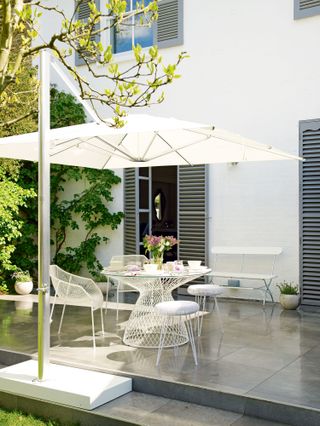 white parasol over paving and white outdoor table and chairs