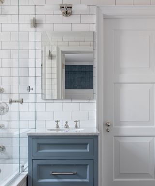 A bathroom with blue vanity, marble-style sink and white subway-tiled walls