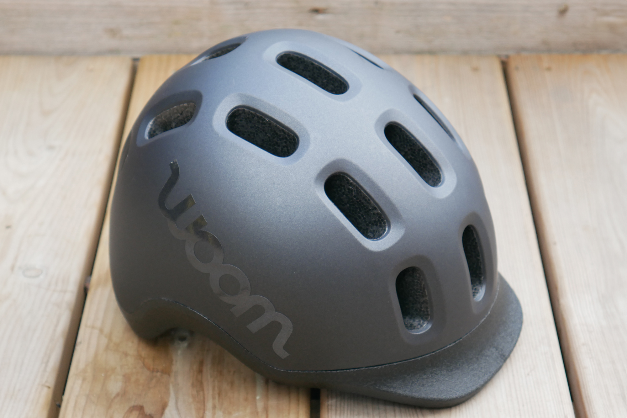 Top down view of the Woom Ready Kids Bike Helmet in black against a back drop of a wooden deck
