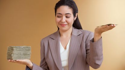 A woman compares a big stack of money in one hand vs. a smaller stack of money in the other.