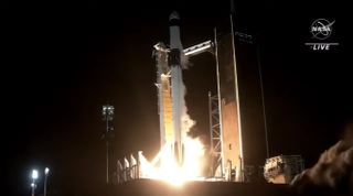 A white and black rocket launches into the nighttime sky