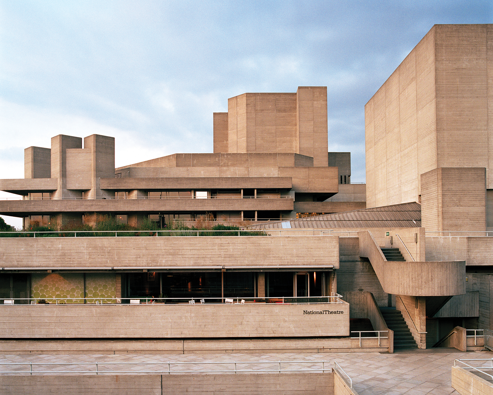 A concrete modernist building of the National Theatre, showcasing distinct geometric shapes and multiple levels under a cloudy sky