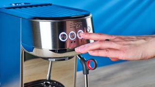 the breville bambino plus / sage bambino plus in stainless steel silver photographed against a blue background shown with its accessories including milk jug, tamper, portafilter, and shown in use extracting espresso