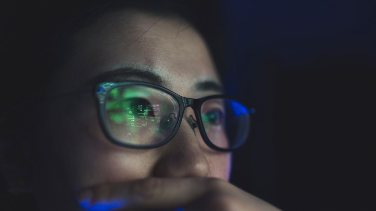 Somebody with glasses thinking while looking at a screen in a dark room