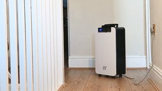 White and black Netta dehumidifier on castors on a landing with wooden floor, plugged in beside white banisters