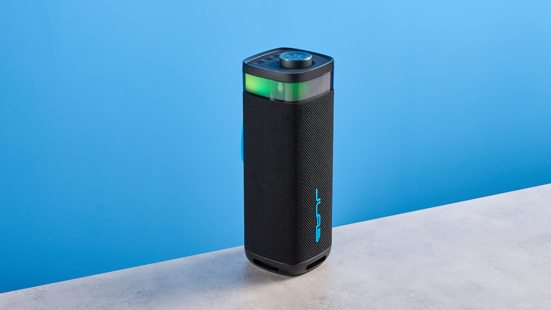 the jlab jbuds party speaker with LED rainbow lights photographed against a blue background