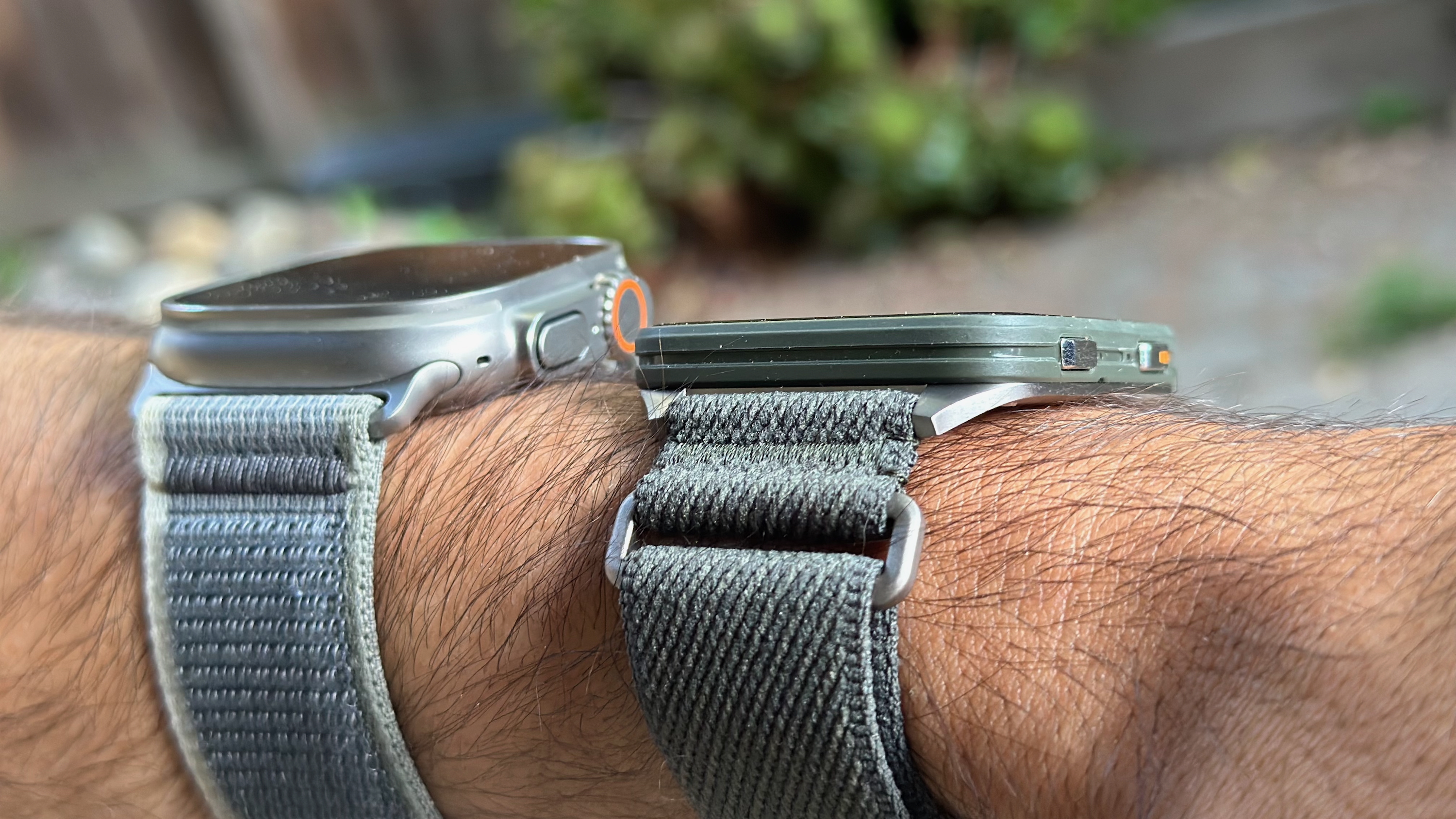 The Apple Watch Ultra 2 (left) and Garmin Venu X1 (right), both worn on one wrist, showing the two watches' comparative thickness.