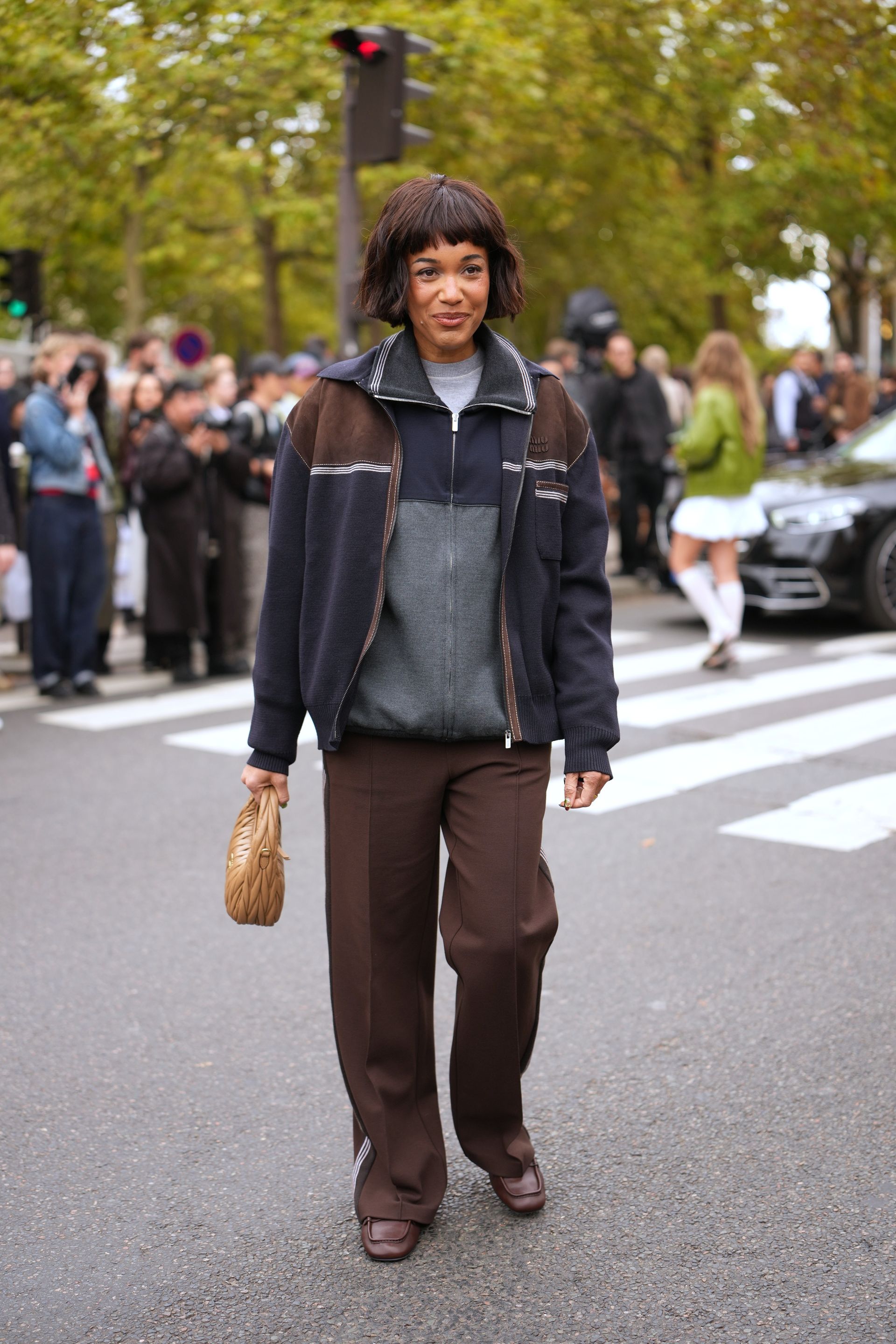 A woman wears a navy and brown jacket, brown pants, and brown loafers.