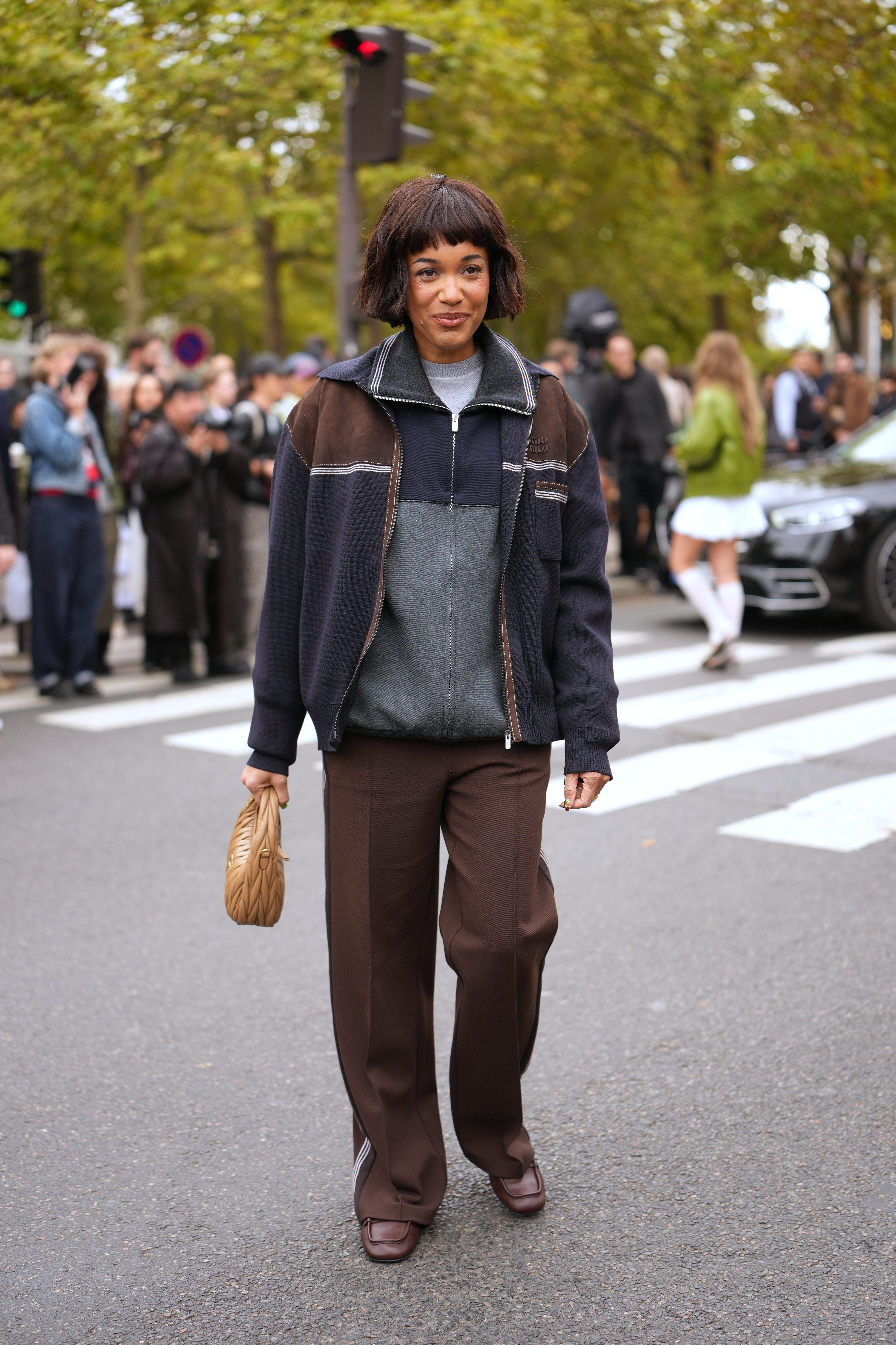 A woman wears a navy and brown jacket, brown pants, and brown loafers.