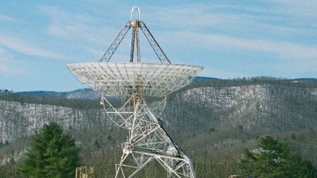 a radio antenna dish points toward the blue sky above a mountain ridge